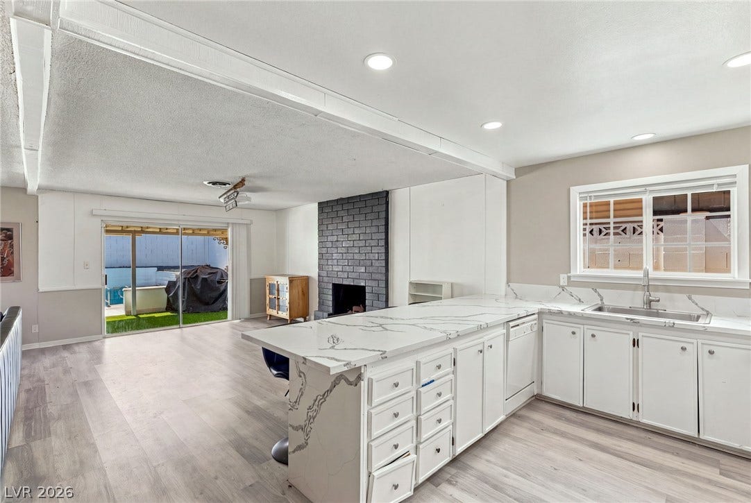 An open floorplan seamlessly connects the stone-countertop kitchen to the adjacent fireplace-centered living area.