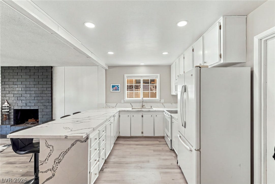 An open kitchen layout pairs seamless quartz countertops with recessed ceiling lights and wood-finish flooring.