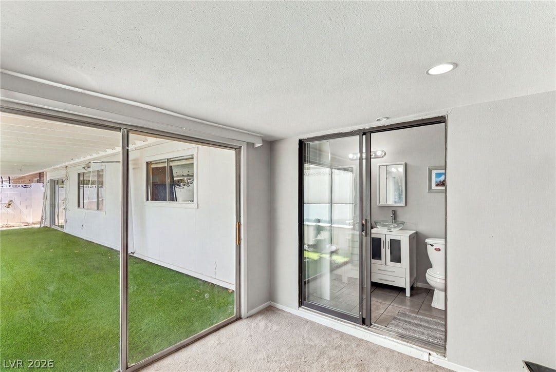 Sliding glass doors connect carpeted interiors with a modern bathroom and grassy outdoor spaces.