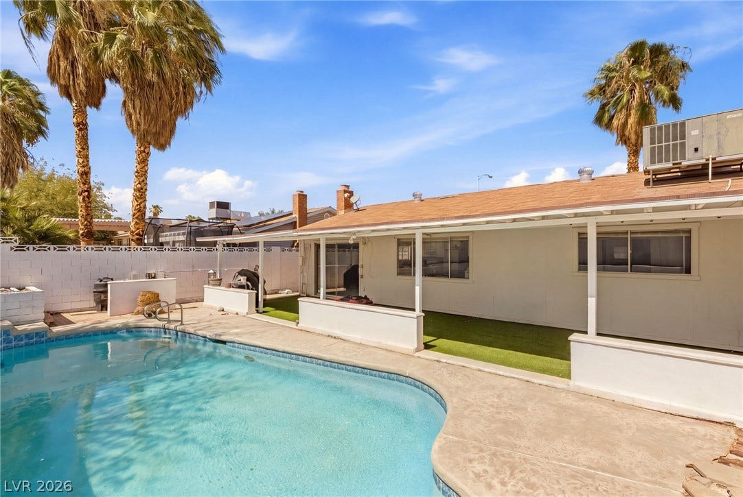A covered patio overlooks a private pool set against a backdrop of mature palm trees.