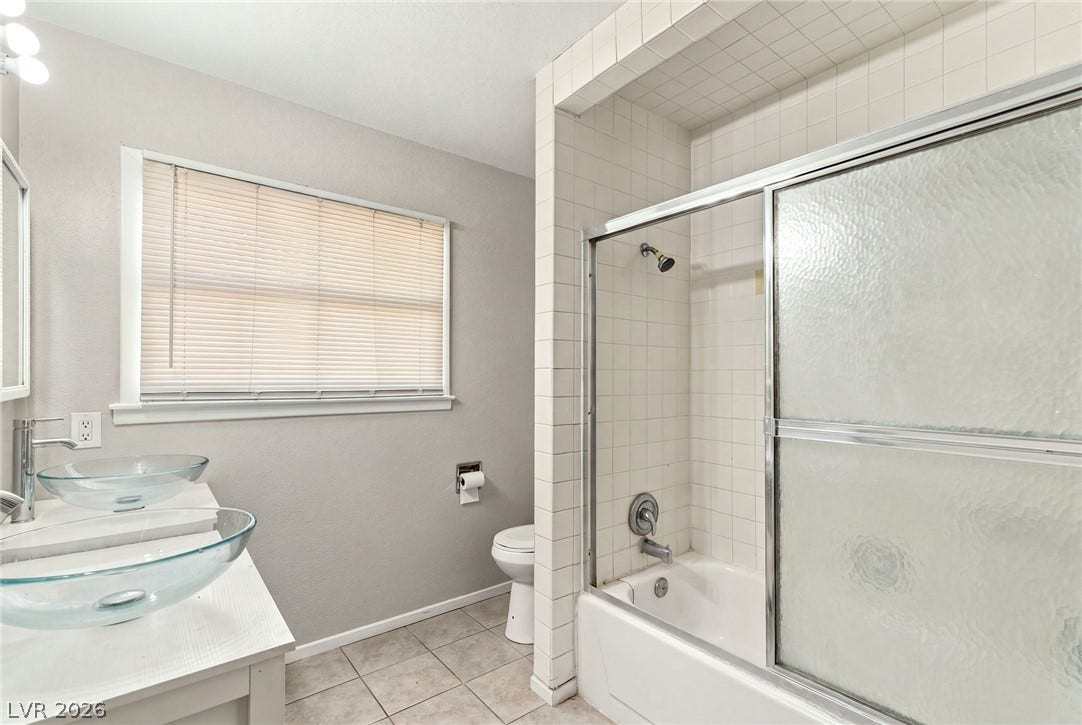 Tiled shower and tub combination stands adjacent to a vanity featuring modern vessel sinks.