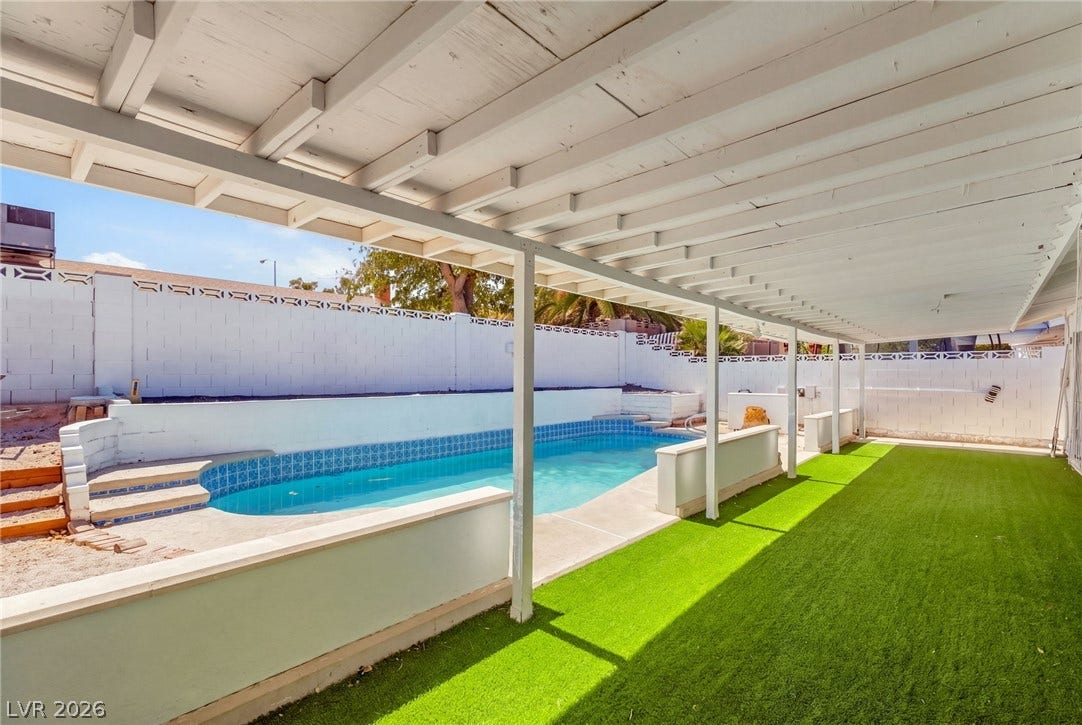 An inviting covered patio overlooks the sparkling swimming pool and a neat lawn area.