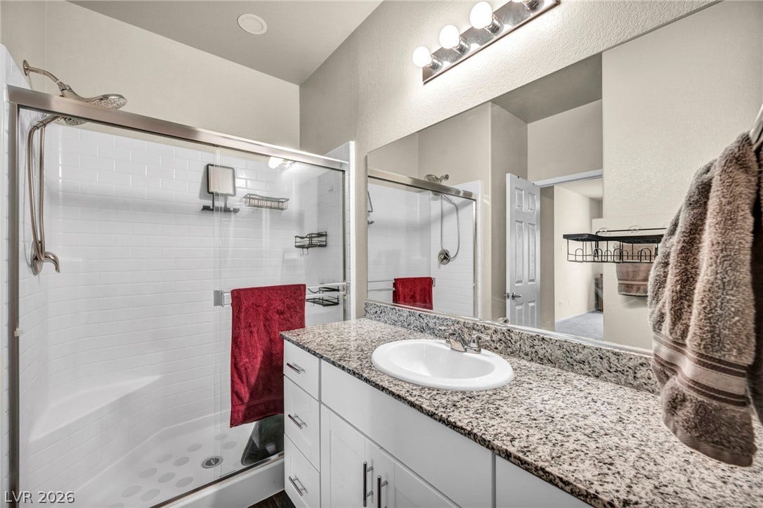 A modern vanity with stone counters stands alongside a glass-enclosed walk-in shower.