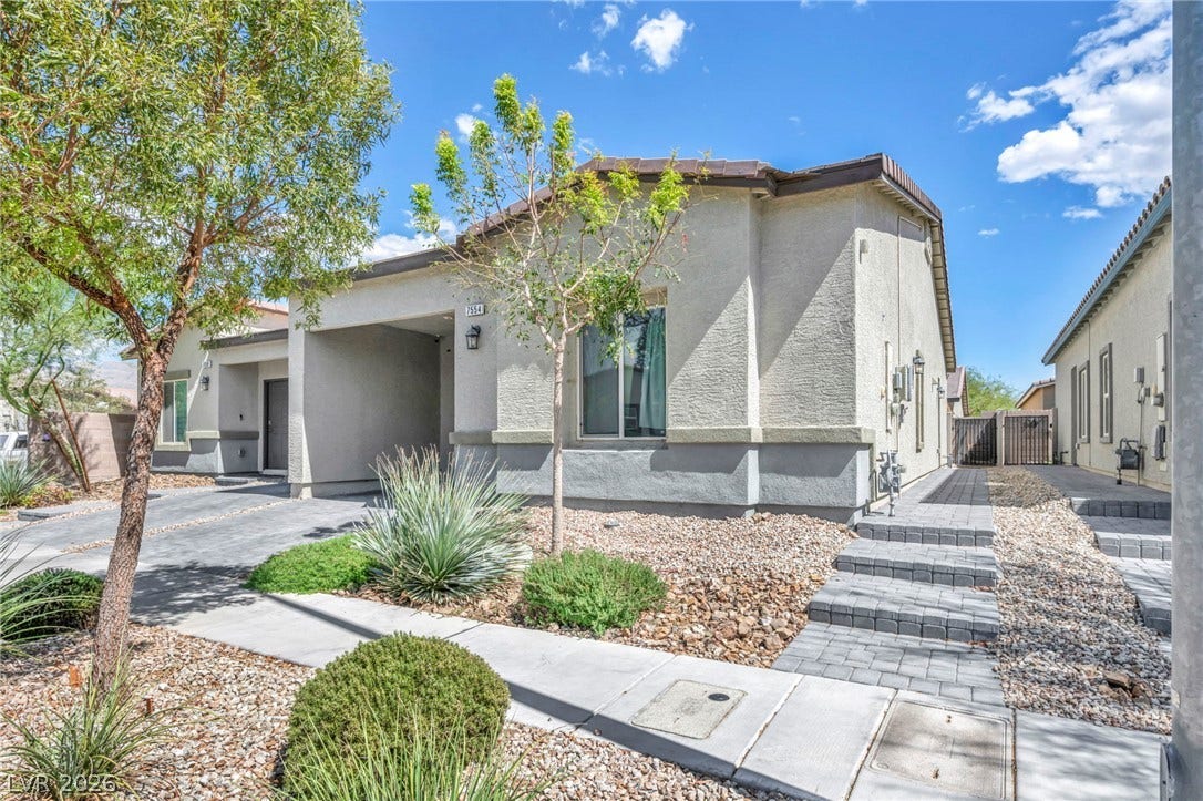 Desert plantings frame a modern stucco home featuring paved walkways under clear desert skies.