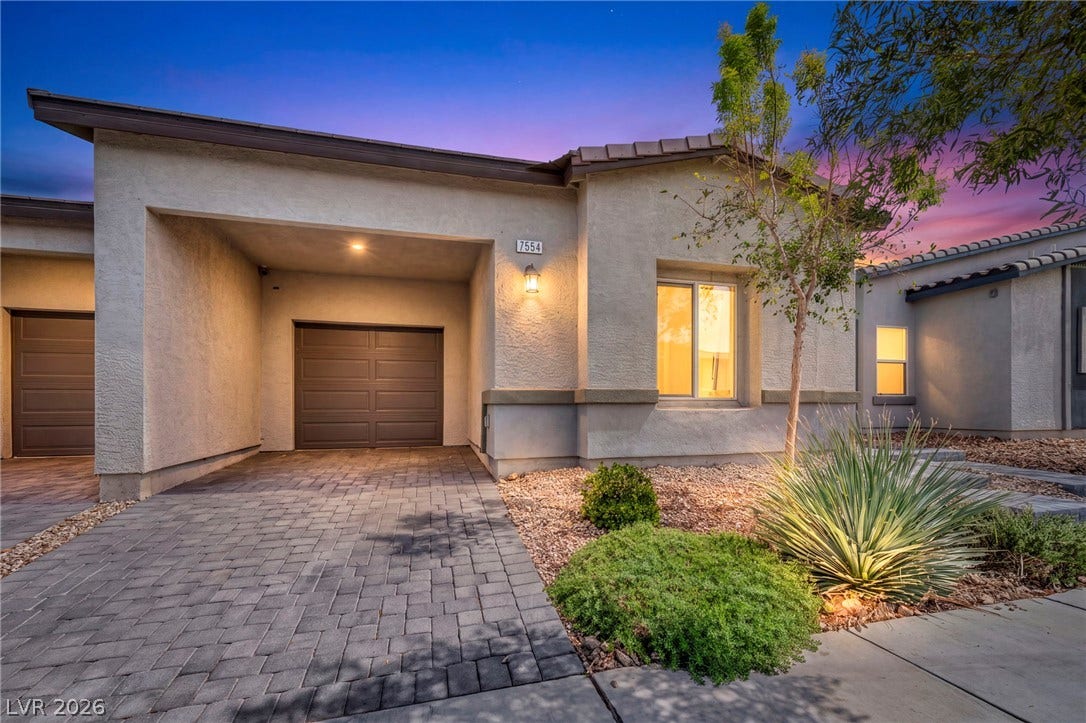 Modern stucco exterior exhibits a clean facade and a beautifully paved driveway under twilight skies.