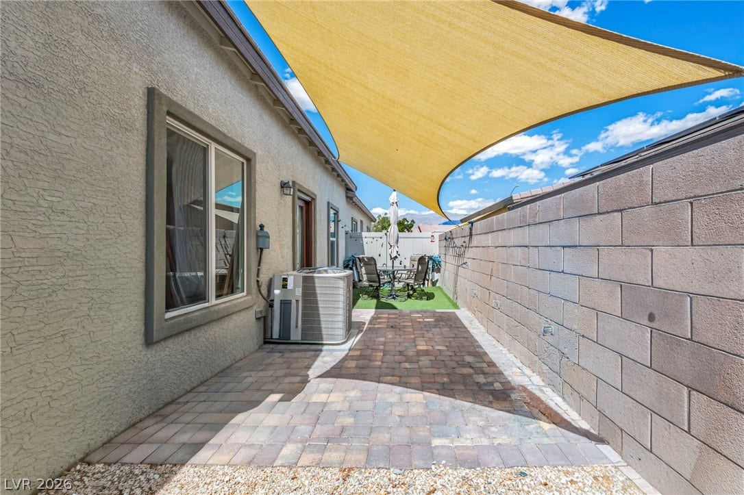 A paved patio area sits shaded by a large sail canopy alongside a block wall.