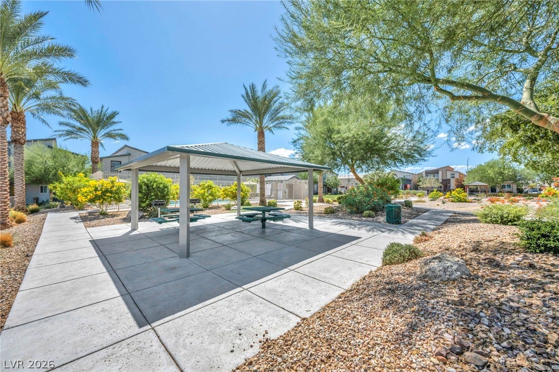 Concrete walkways lead to a shaded pavilion amid mature desert landscaping.