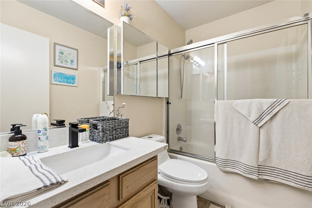 1747 Ashburn Drive, North Las Vegas, NV 89032 A classic bathroom layout pairs a wooden vanity with a sliding glass tub enclosure.