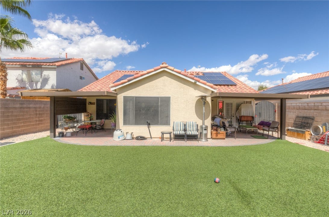 1747 Ashburn Drive, North Las Vegas, NV 89032 A spacious covered patio overlooks a manicured green lawn framed by secure perimeter fencing.
