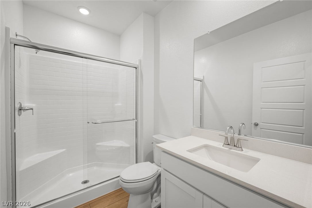 8142 Gusty Brook Street, Las Vegas, NV 89113 A modern bathroom features a clean glass-enclosed shower alongside a stone-topped vanity.