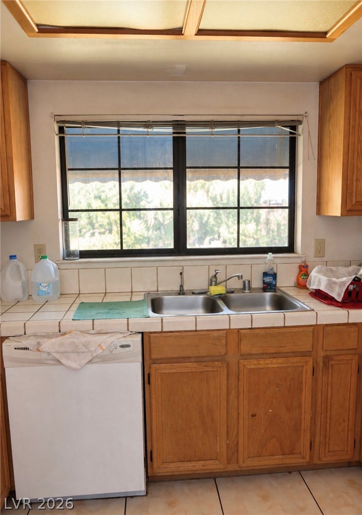 101 Luna Way, #242, Las Vegas, NV 89145 Tiled countertops frame a double-bowl sink beneath a wide window overlooking outdoor greenery.