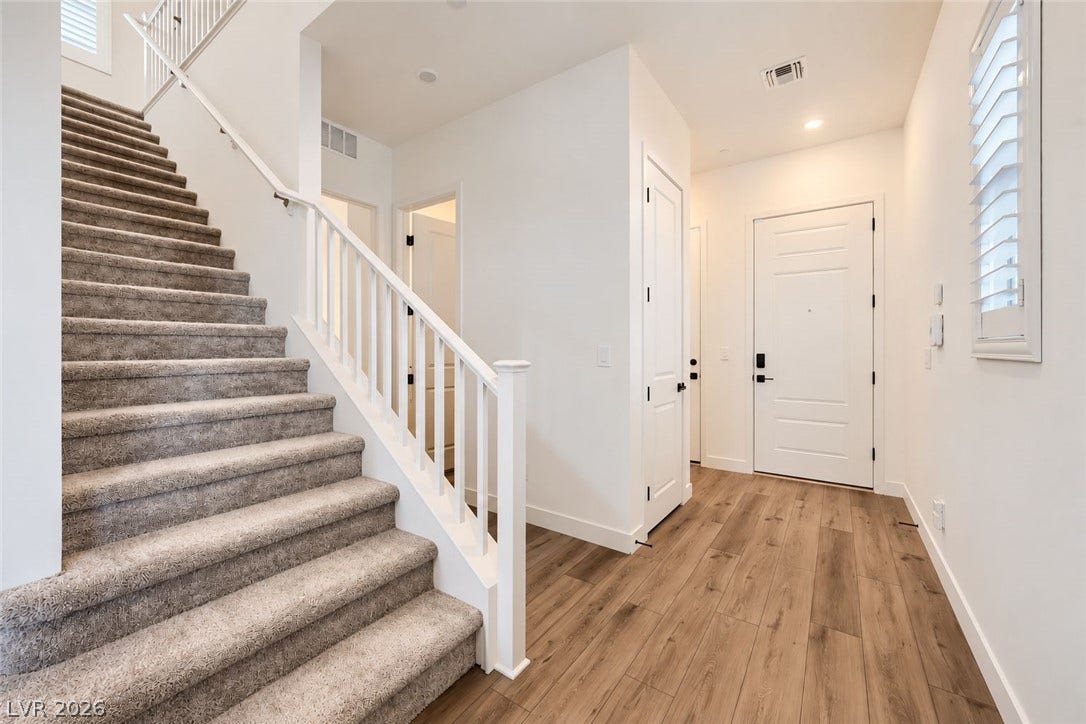 An inviting entryway leads directly to a carpeted staircase and wood-style flooring.