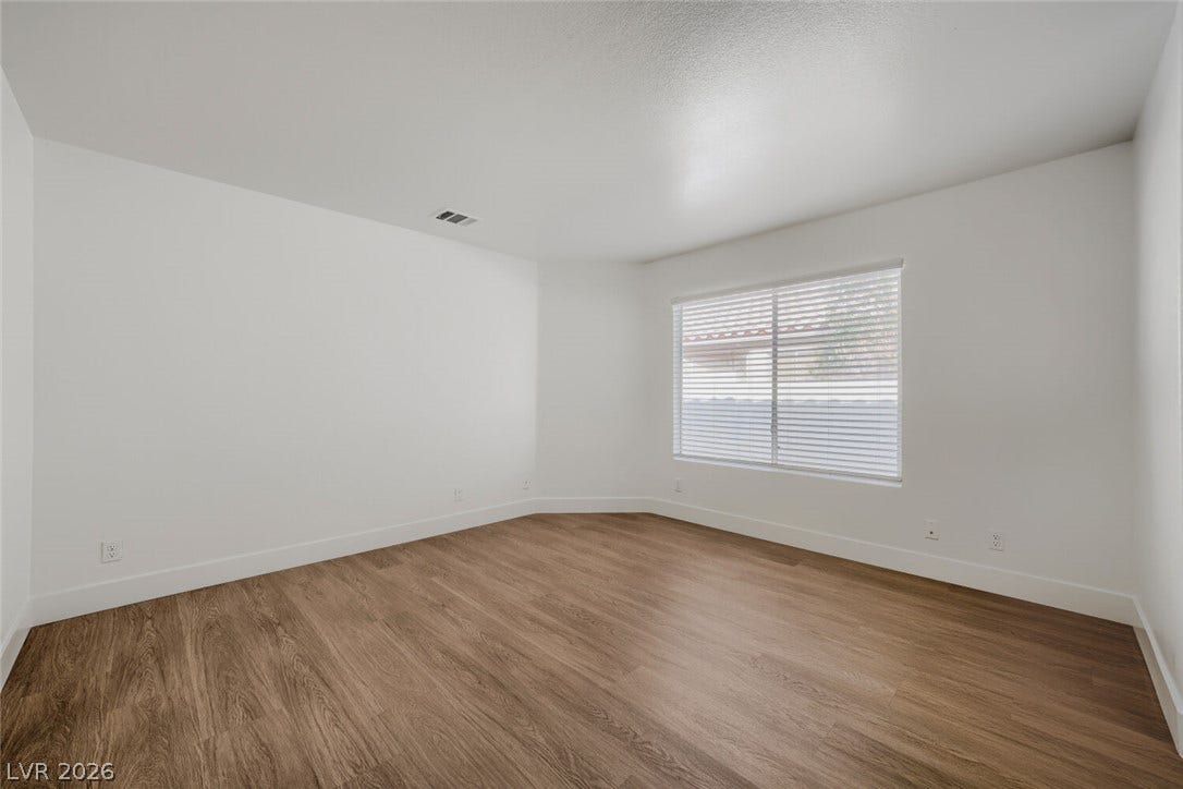 5736 Baffy Circle, Las Vegas, NV 89142 A spacious bedroom features rich wood-look flooring and a wide window with integrated blinds.