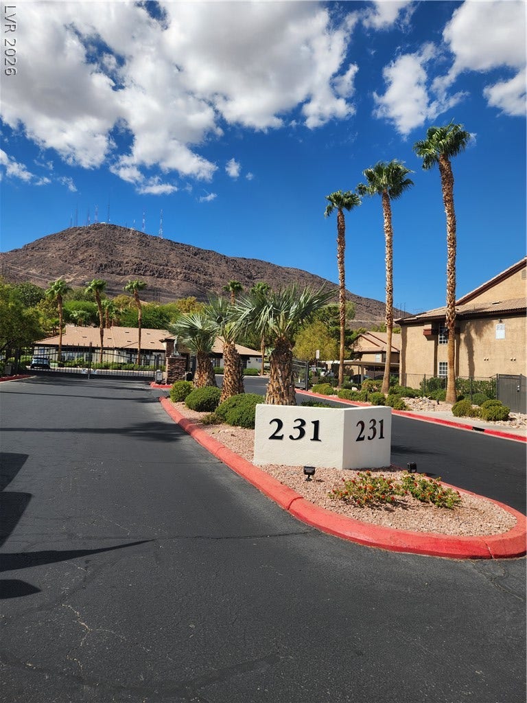 231 W Horizon Ridge Parkway, #924, Henderson, NV 89012 Towering palm trees frame the gated entrance set against a dramatic desert mountain backdrop.