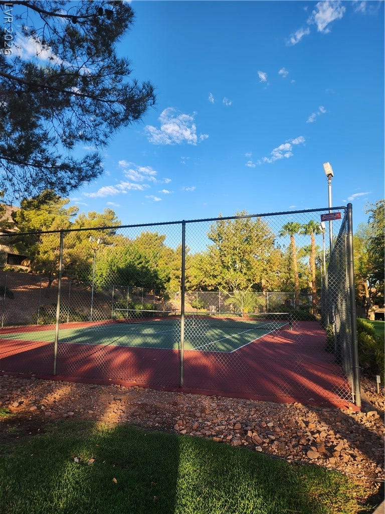 231 W Horizon Ridge Parkway, #924, Henderson, NV 89012 A private tennis court is nestled among mature trees under a clear blue sky.