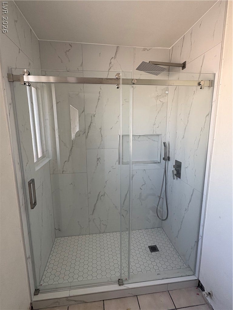 Elegantly veined marble-look tile walls highlight a modern walk-in shower with sliding glass doors.