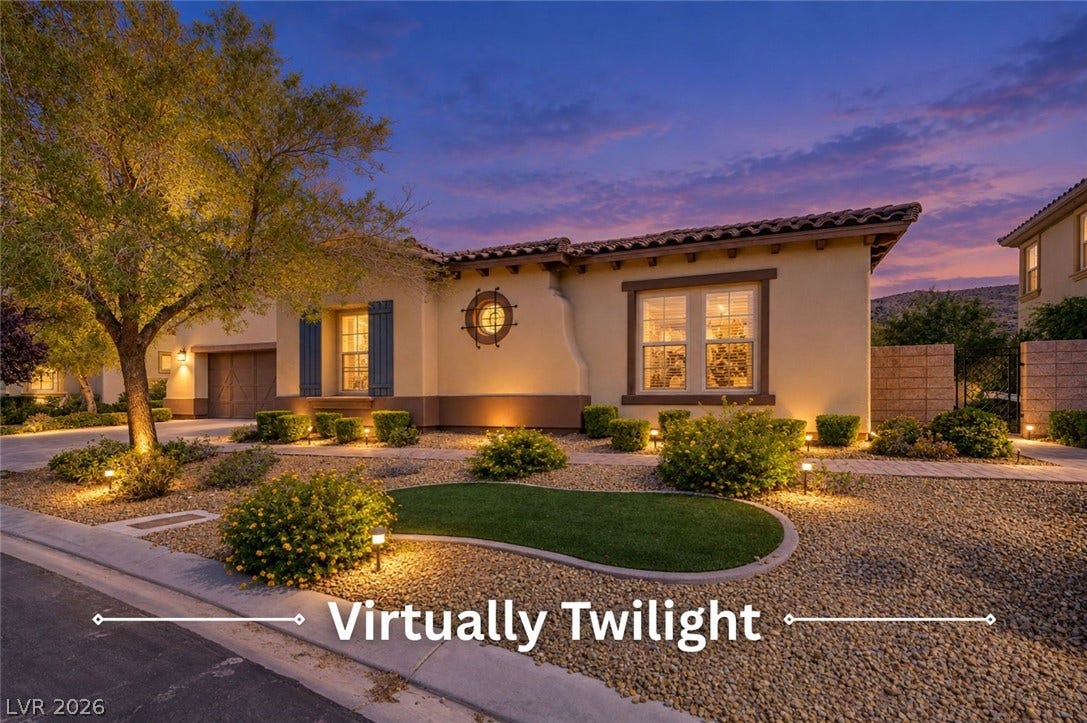 Warm exterior illumination showcases the Spanish tile roof and desert landscaping of this modern home.