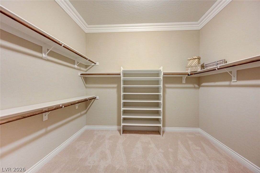 Crown molding and plush carpeting define this structured walk-in closet space.