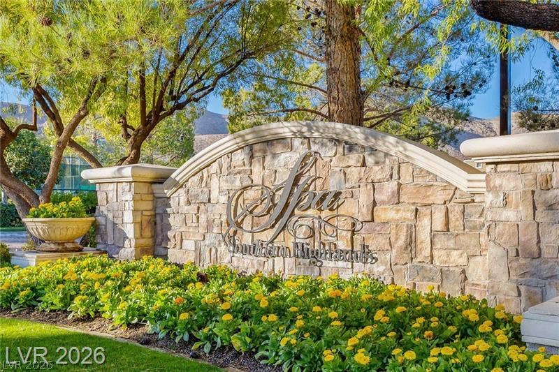 Mature trees frame the stone monument sign surrounded by meticulously landscaped flower beds.