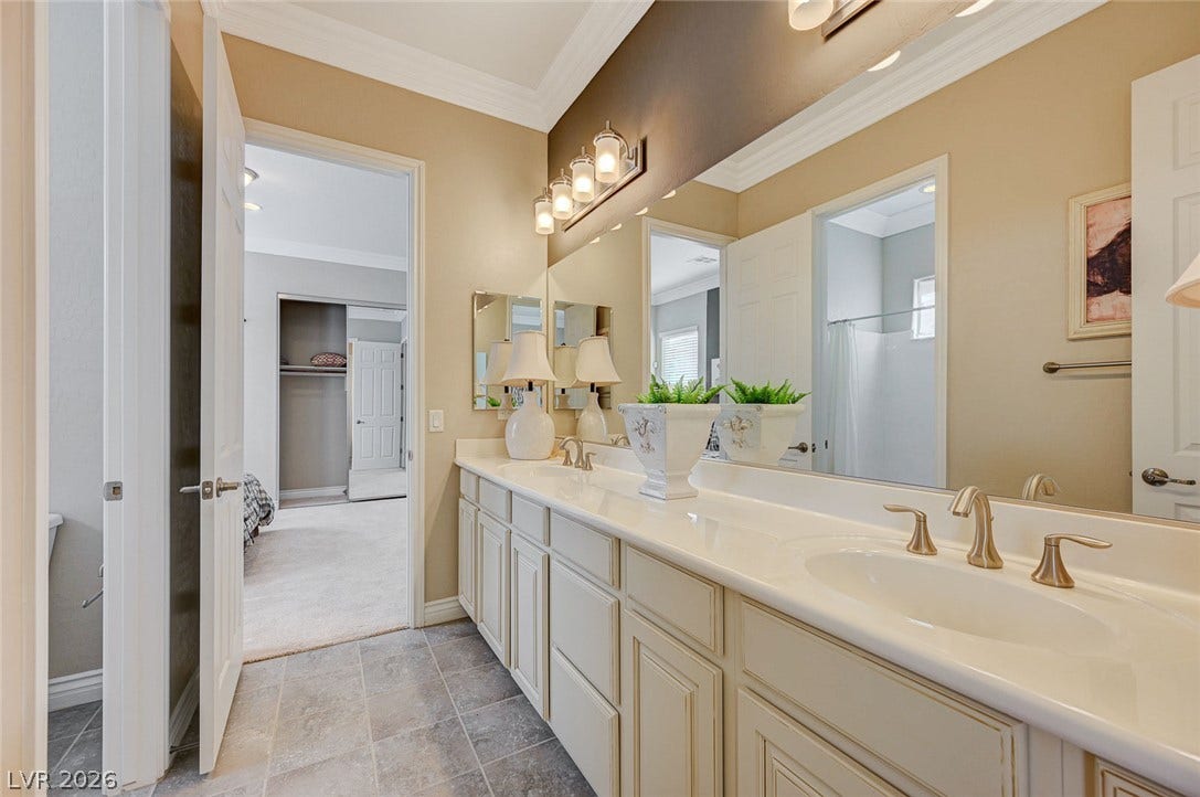 Elegant crown molding complements a dual-sink vanity and classic tiled flooring in this bright space.