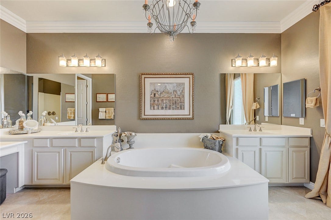 Ornate crown molding and elegant light fixtures elevate this main bath with dual vanities.