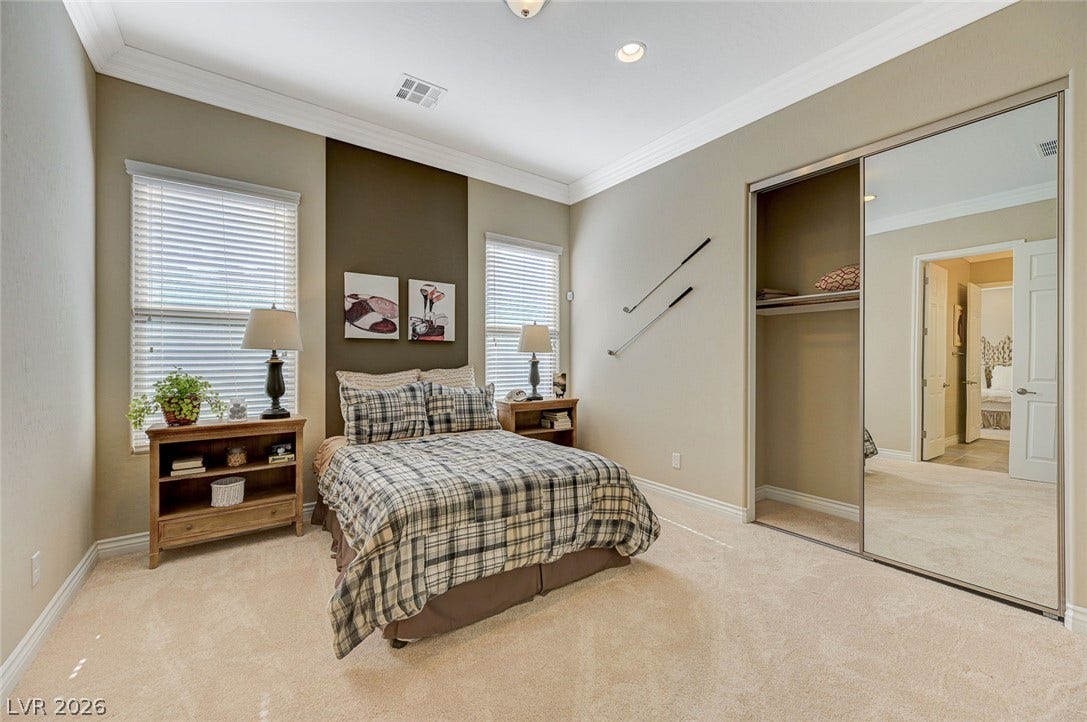 High ceilings and elegant crown molding elevate this carpeted bedroom featuring sliding mirrored closets.