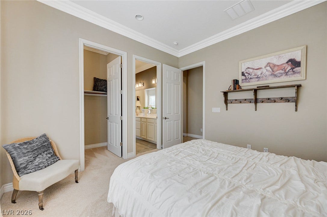 Thick crown molding frames the recessed lighting above soft carpeting in this comfortable bedroom.