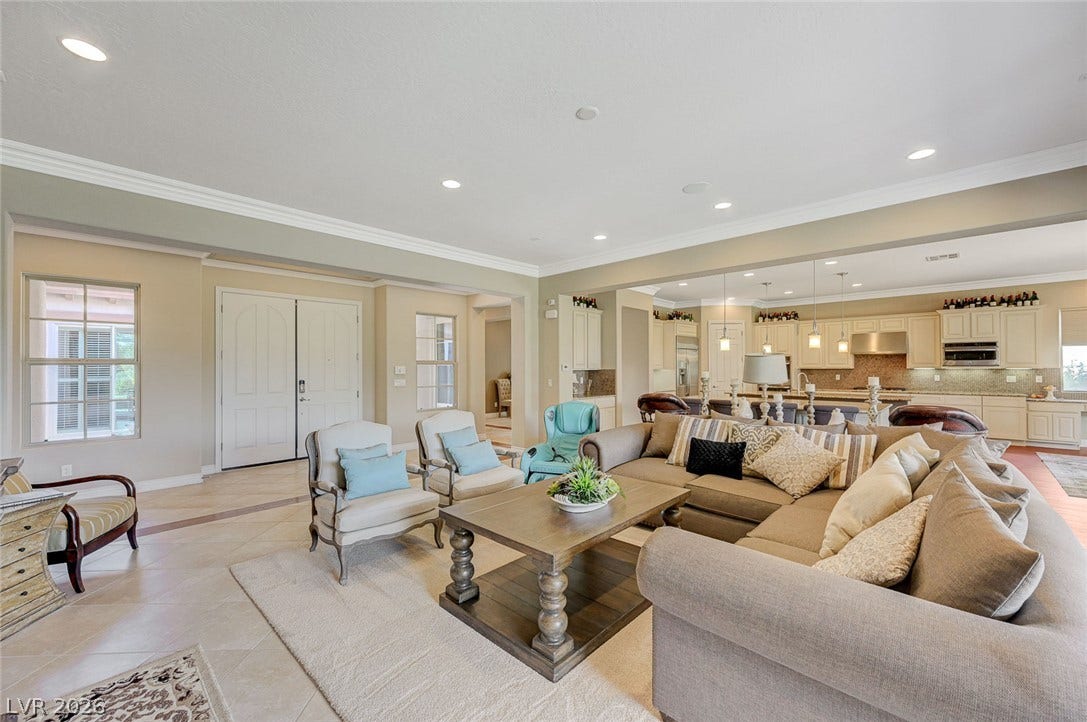 Crisp crown molding and recessed lighting frame this airy, open-concept living space with tile flooring.