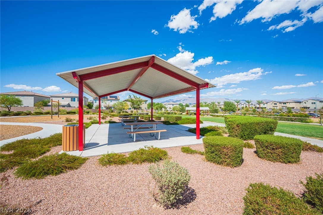 An outdoor pavilion with picnic tables sits nestled within a beautifully landscaped neighborhood park.