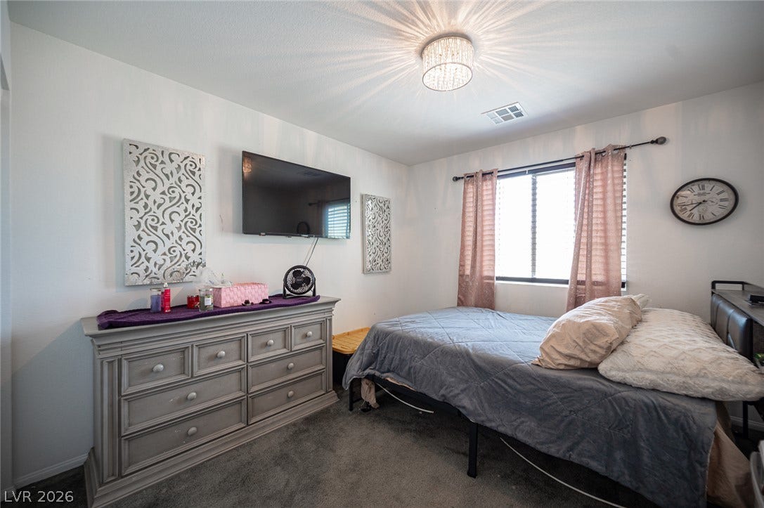 Soft carpeting underfoot anchors a cozy bedroom filled with natural light from a wide window.