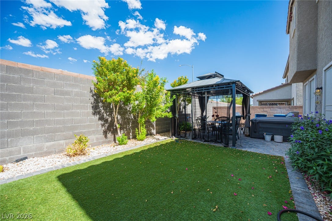 A private lawn area sits alongside a paved patio beneath a structured backyard gazebo.