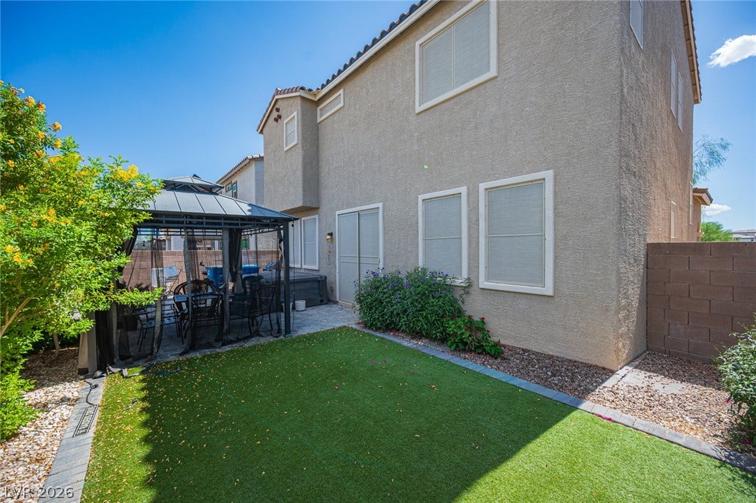A private backyard lawn sits adjacent to the stucco home and covered patio space.