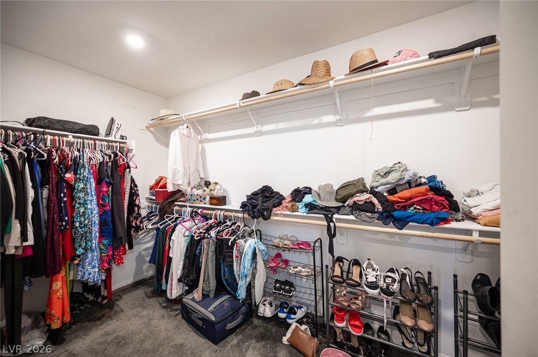An organized walk-in closet boasts recessed lighting and carpet flooring.