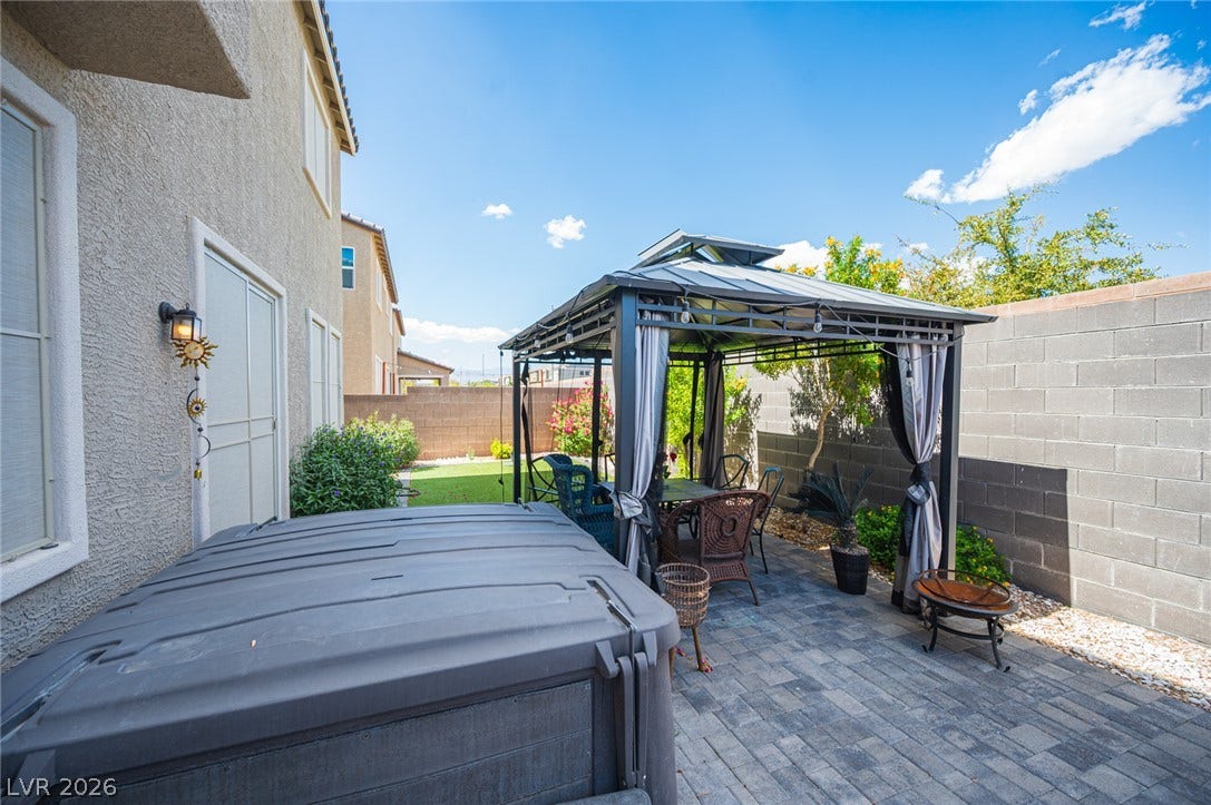 An inviting backyard patio features stone paving, a protective gazebo, and a private hot tub.
