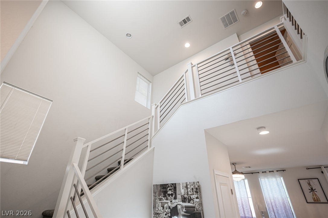 A staircase with modern railings ascends to the upper level under high ceilings.
