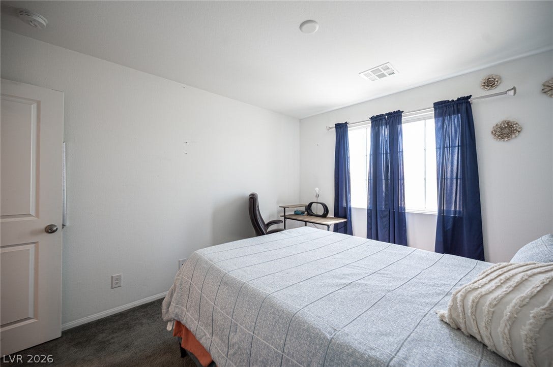 Sunlight streams through the wide window into this comfortable bedroom with soft carpeting.