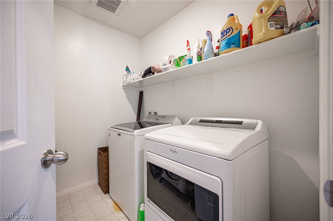 A functional laundry space features durable vinyl tile flooring and a long storage shelf.