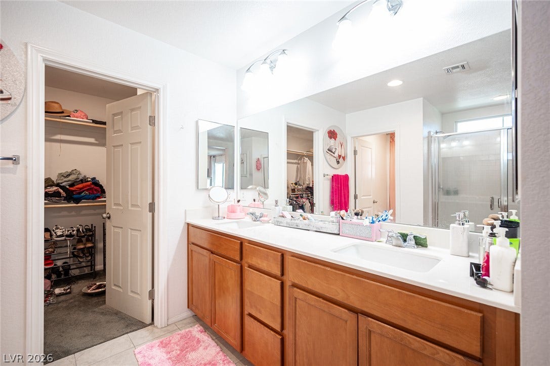 Double vanities with warm wood cabinetry stand adjacent to a spacious walk-in closet.