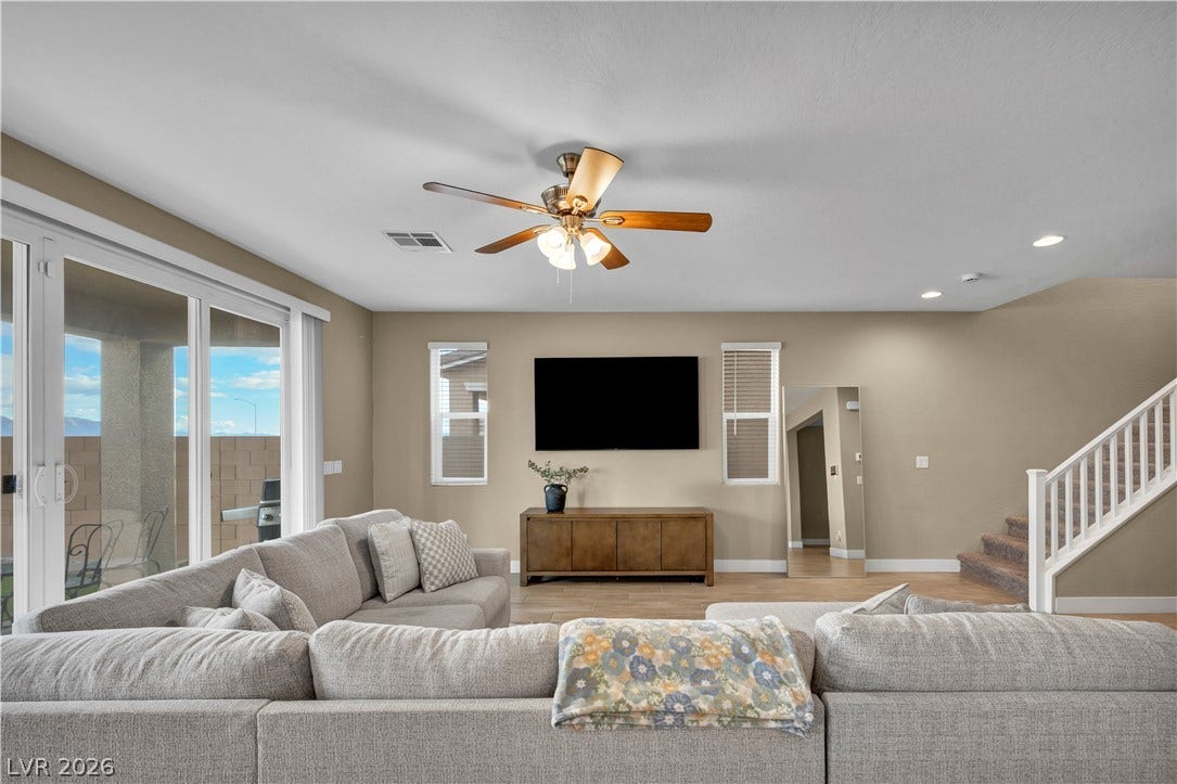 7128 Port Stephens Street, North Las Vegas, NV 89084 Sunlight streams through sliding glass doors into a spacious living room featuring wood-look tile floors.