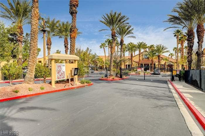 2300 E Silverado Ranch Boulevard, #1077, Las Vegas, NV 89183 Secure gated access reveals a palm-lined entrance leading toward the neighborhood community.