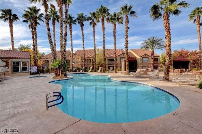 2300 E Silverado Ranch Boulevard, #1077, Las Vegas, NV 89183 Palm trees frame a sparkling community pool lined with lounge chairs.
