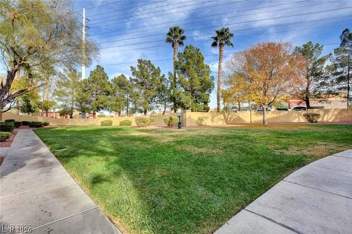 2300 E Silverado Ranch Boulevard, #1077, Las Vegas, NV 89183 Paved sidewalks frame a green community lawn lined by mature trees and palms.