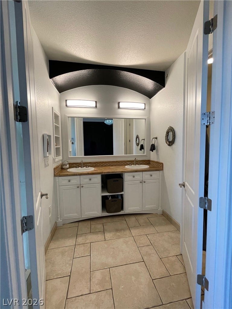 30 Via Vasari, #102, Henderson, NV 89011 An arched architectural detail frames the double vanity and tile flooring in this primary bathroom.