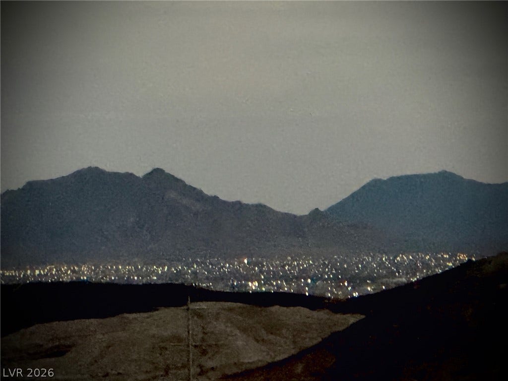 30 Via Vasari, #102, Henderson, NV 89011 Distant city lights shimmer below rugged mountain peaks under a twilight sky.