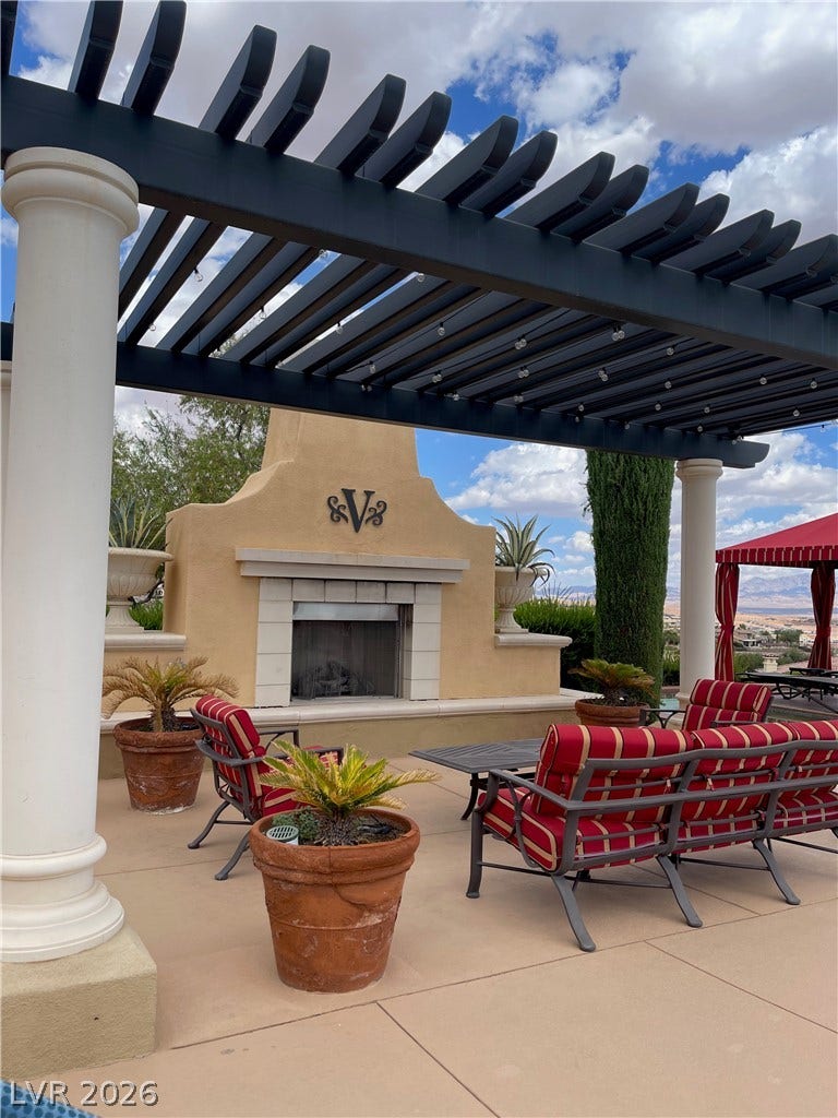 30 Via Vasari, #102, Henderson, NV 89011 An inviting outdoor fireplace warms a spacious concrete patio sheltered beneath a classic dark pergola.