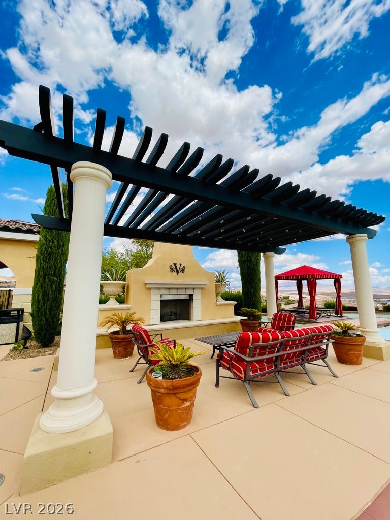 30 Via Vasari, #102, Henderson, NV 89011 An inviting concrete patio features a dark-stained pergola and an outdoor fireplace under clear skies.
