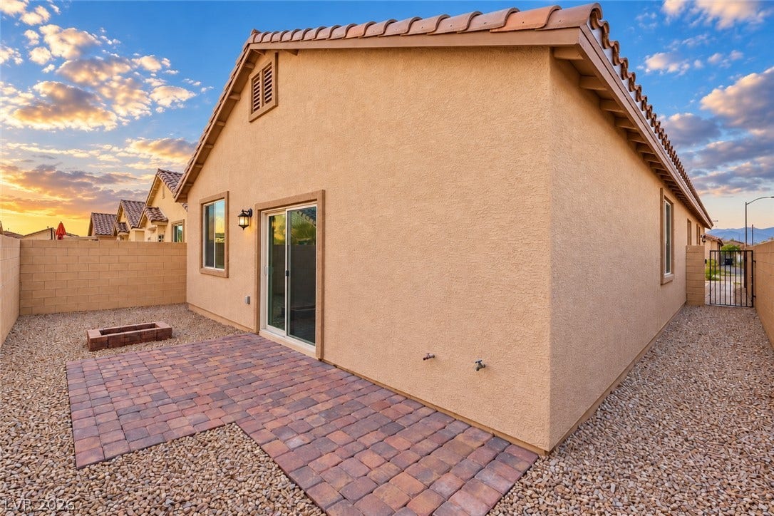 5740 Saltrock Grove Street, North Las Vegas, NV 89081 A paved patio and gravel yard line the back of this stucco home under sunset skies.