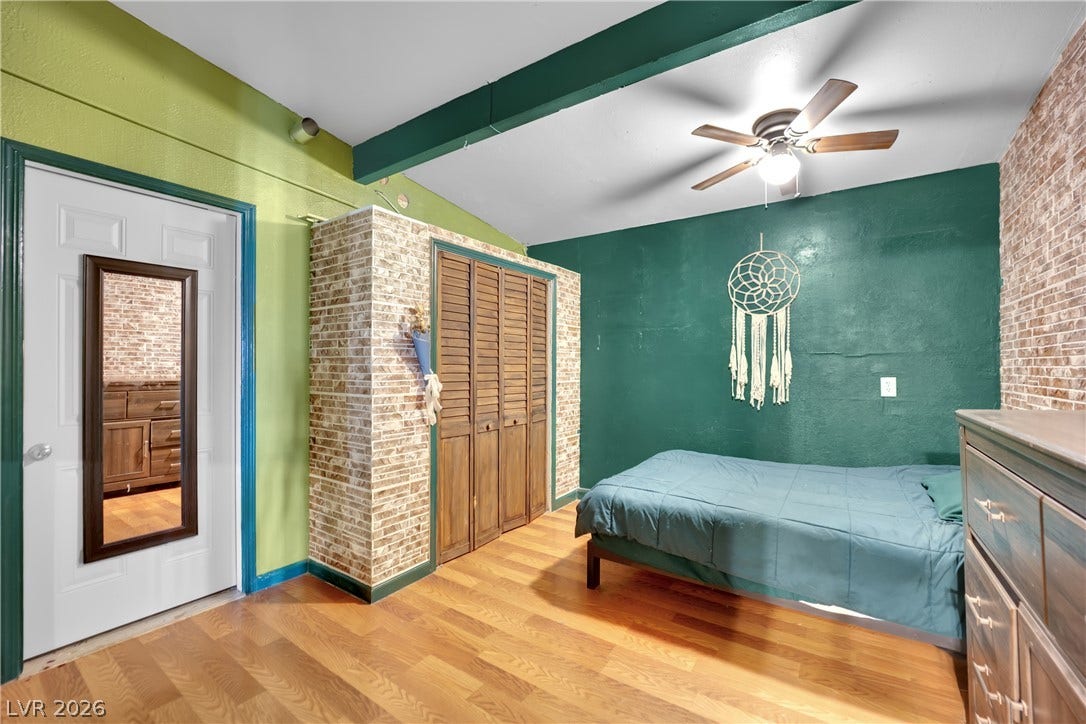 Exposed beams accent the ceiling of this cozy bedroom with rich wood flooring.
