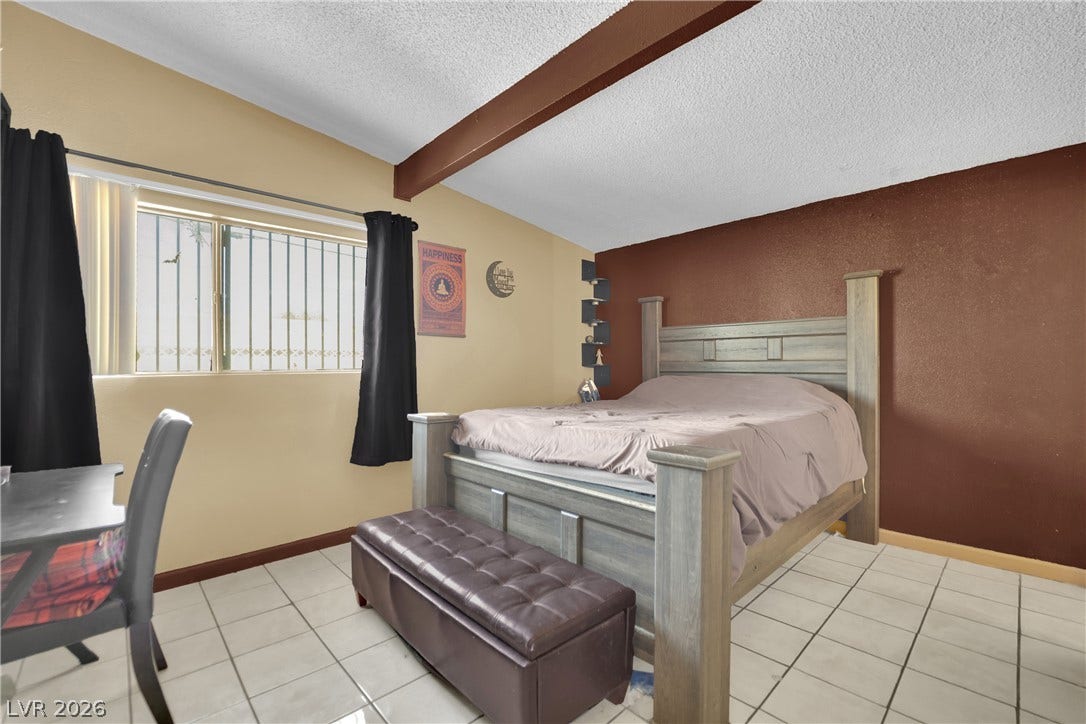 Tiled flooring and a vaulted ceiling with an exposed wood beam detail this bedroom.