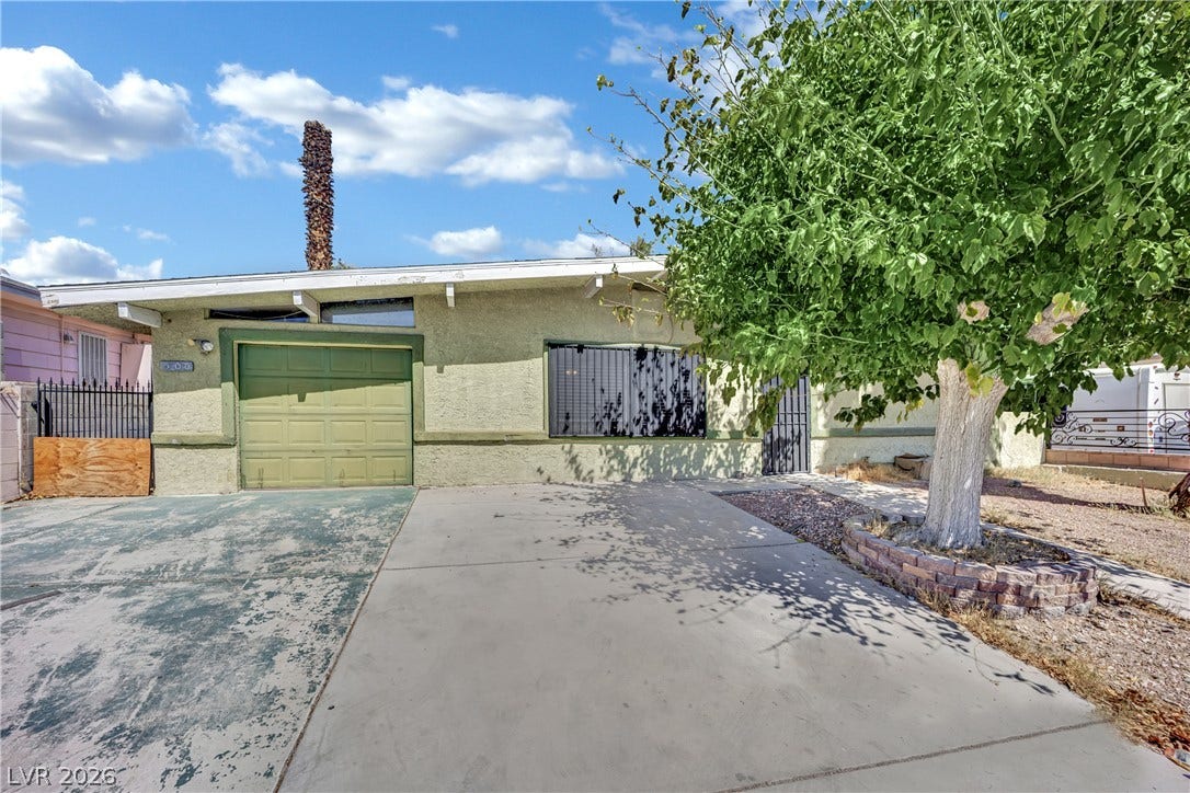 A classic stucco exterior features a concrete driveway and mature shade tree.